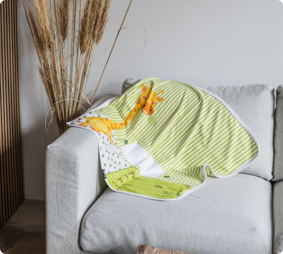 Eine Babydecke mit einem Giraffen-Design liegt auf einer Couch